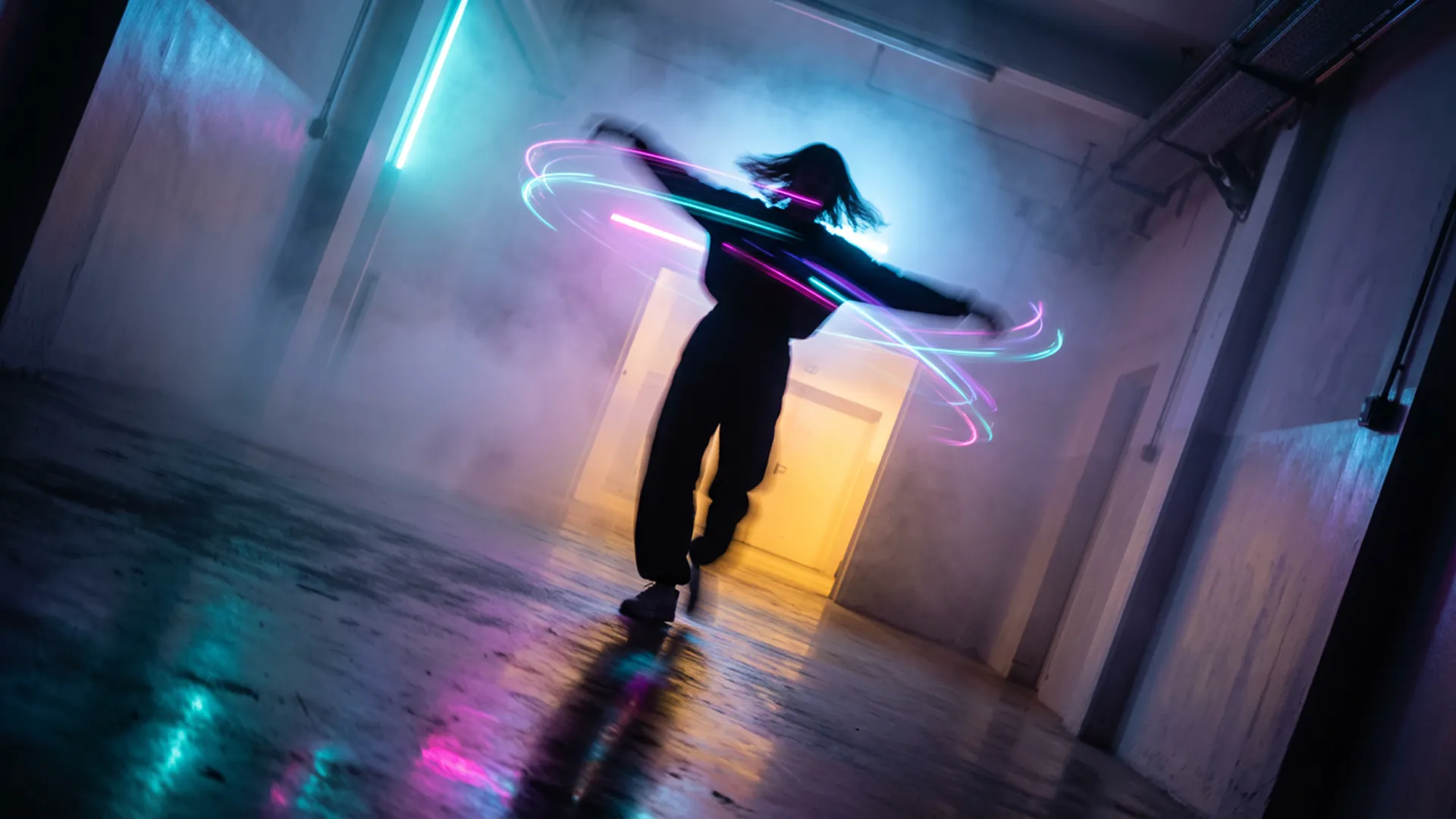 In a burst of uninhibited movement, a figure is captured mid-spin in a corridor of light and mist. The photography freezes the action at its peak, the person's arms flung wide, their head tilted back in a moment of pure, kinetic release. This rapid twirl has visibly disturbed the dense, colored fog, creating eddies and vortices of cyan, magenta, and violet light around their silhouetted form. The composition is vibrant and chaotic, a stark contrast to a static scene. Light from a warm, yellow-orange portal ahead illuminates the swirling mist from one direction, while a cool blue glow from behind adds depth and complexity to the color palette. The floor, a dark mirror, reflects a blurred, chaotic version of the sceneβa painterly smear of motion and color. The camera angle is slightly tilted, a Dutch angle that enhances the feeling of disequilibrium and exhilaration, capturing a fleeting, joyful rebellion against the quiet, contemplative nature of the space